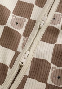 Close-up of a white zipper on ribbed fabric with a brown and beige bear face pattern.