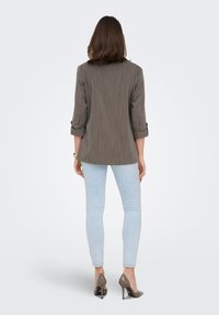 Blazer rayé gris à manches retroussées, associé à un jean skinny bleu clair et des chaussures à talons beiges. Vue de dos avec une texture minimale.