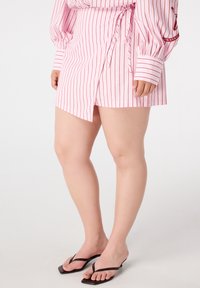 Jupe enveloppante rayée rose et blanche en tissu léger, avec un lien à la taille et une fente haute sur un côté.