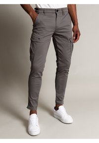 Grijze cargobroek met een slim fit, voorzien van zijzakken en een ritsdetail bij de zoom, gecombineerd met witte sneakers.