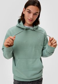 Groene hoodie van zacht materiaal, met een buidelzak, capuchon met trekkoord en geribbelde boorden. Subtiele logo op de borst.