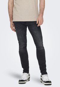 Vaqueros negros de corte ajustado, con un ligero desgaste y efecto de arrugas. Combinados con zapatillas blancas con detalles en negro.