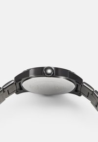Schwarze Metallarmbanduhr mit einem eleganten, runden Gehäuse, einem glatten Glanzglas und einem metallischen Armband mit einzelnen Gliedern. Große Krone an der Seite.