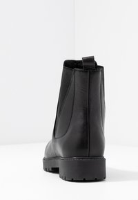 Svart läderankelboots med elastiska sidopaneler och en dragflik baktill. Har en texturerad sula för bra grepp. Enkel, stilren design.