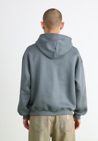 Grå hættetrøje med hætte, afslappet pasform, ribbede manchetter og kant. Båret med lyse beige bukser, som viser et simpelt, afslappet design.
