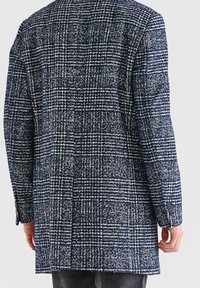 Marineblauwe geruite jas met een textuurrijke, geweven stof. Lange mouwen met knoopaccenten en een midilange snit voor dekking.