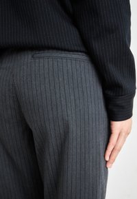 Gray pinstripe trousers made of smooth fabric, featuring a tailored cut, side pocket, and a waistband with a sleek, minimalist design.