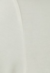 Vaaleanbeige raitakangas, jossa on sileä pinta, hieman vartalonmyötäinen muotoilu ja näkyvä sauman yksityiskohta toisella puolella.