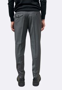 Pantaloni grigi su misura con una texture liscia, dotati di due tasche posteriori e un design a taglio slim. Indossati con scarpe nere.