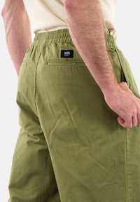 Pantalones verde oliva con cintura elástica y bolsillos laterales. Cuenta con una etiqueta de Vans en la parte posterior. Tela suave con acabado mate.