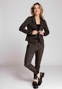 Schwarzer Anzug mit feinen goldenen Linien, taillierte Jacke und schmal geschnittene Hose, kombiniert mit schwarzen Lederloafers. Glatte Textur, modernes Design.