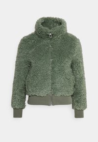 Grön faux fur-jacka med hög krage, dragkedjestängning, ribbad nederkant och armbågar. Texturerad yta med en fluffig utseende.