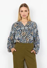Blusa blu e beige a fantasia con maniche lunghe e scollatura a V, abbinata a pantaloni olive verdi a vita alta. Tessuto morbido.