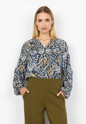 Blå och beige mönstrad blus med lång ärm och V-ringning, tillsammans med högmidjade olivgröna byxor. Slät tygtextur.