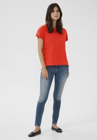 Haut rouge à manches courtes avec des accents de boutons argentés sur les épaules, associé à un jean skinny bleu et des ballerines noires. Tissu doux, coupe décontractée.