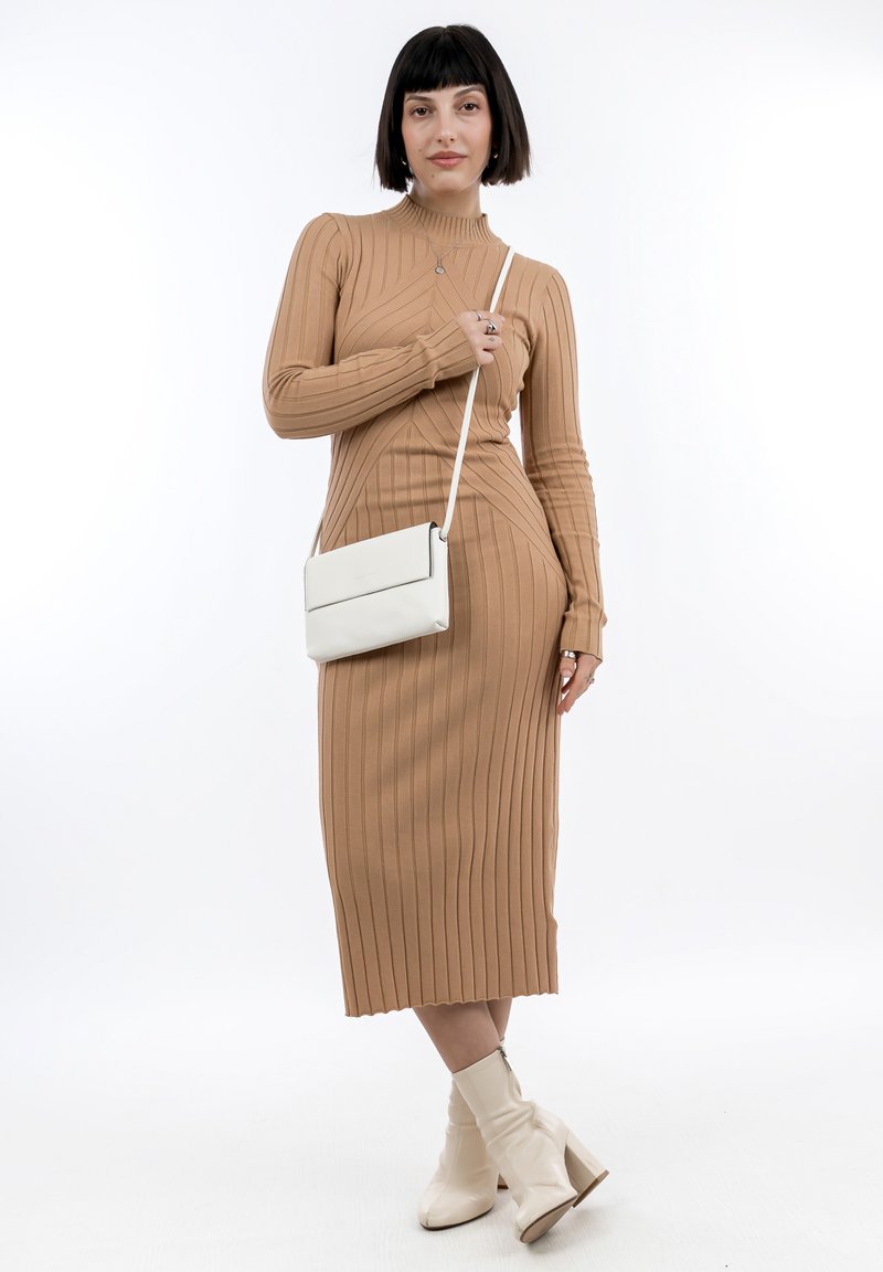 Vestido ajustado de manga larga y canalé en color tostado con cuello alto. Combinado con un bolso cruzado blanco y botas de tobillo en color crema. Presenta patrones sutiles.