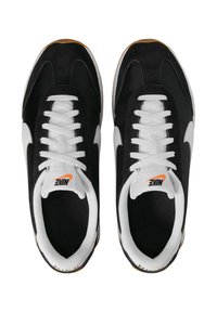Baskets noires et blanches en matériaux daim et maille, dotées de lacets blancs et d'un logo Nike orange sur la languette. Semelle en caoutchouc.