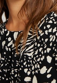 Blůza s černobílým vzorem, zaobleným výstřihem, lehkým materiálem a volným designem s abstraktními tvary a texturami.