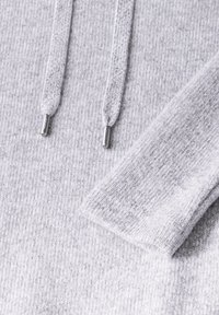 Grå stickad sweatshirt med två dragsnören med metalldetaljer, ribbad textur och en mjuk yta. Accentuerad med en uppvikt ärm.
