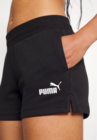Black cotton shorts with a ribbed waistband, side pockets, and a white Puma logo on the lower left leg. Features a split seam design.