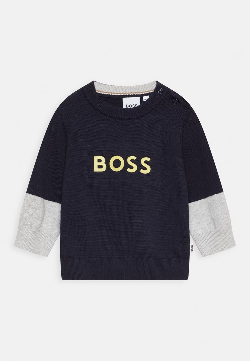 Pull bleu marine pour tout-petit avec poignets gris, col rond, détail bouton à l'épaule et texte "BOSS" en jaune sur le devant.