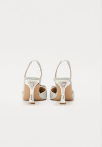 Sølvglitrende høyhælte sandaler med åpen bak, justerbar ankelrem og metallisk detalj på hælen. Glatt beige innersåle.
