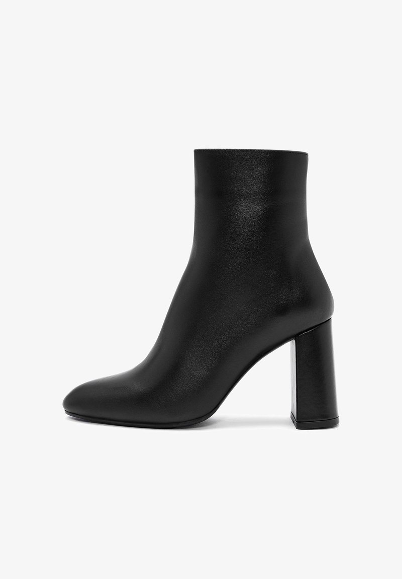 Botín negro de tobillo hecho de cuero suave, con punta afilada y un tacón cuadrado rectangular brillante. Diseño sencillo sin adornos.