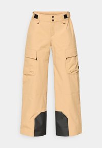 Calças cargo bege com múltiplos bolsos laterais, uma bainha inferior preta e um fecho de gancho e laço na cintura com fecho de botão duplo.