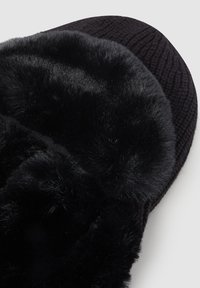 Czarna klapek z miękkim futerkiem z sztucznego futra, teksturowanym materiałem na spodzie, okrągłym kształtem oraz puszystym, wyściełanym designem dla wygody.