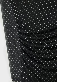 Schwarz gepunktetes Oberteil mit gerafftem Design, langen Ärmeln und einem strukturierten Stoff mit gleichmäßig verteilten kleinen weißen Punkten.