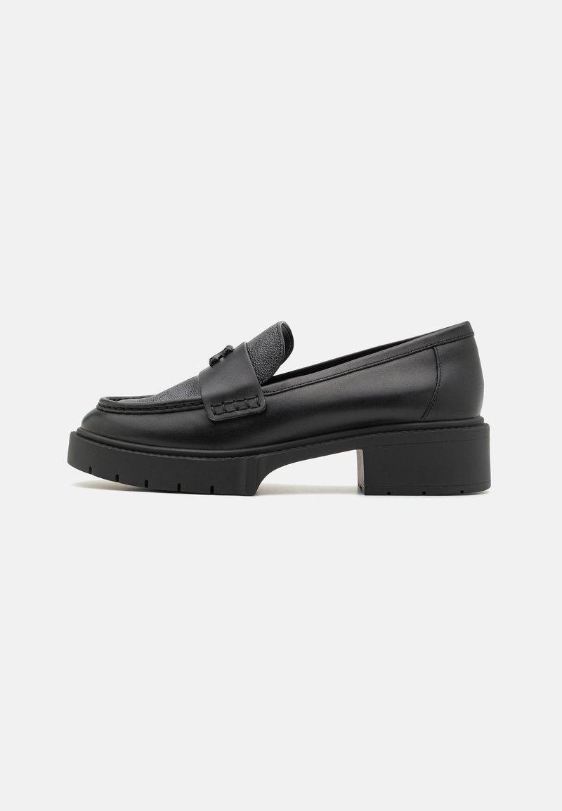 Mocassin en cuir noir avec dessus texturé, pompon décoratif, talon épais et semelle robuste, présenté de profil sur fond blanc.