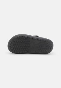 Schwarze Gummisohle mit strukturiertem Profil für besseren Halt, leicht gewölbt an der Zehenpartie und mit flachem Absatz.