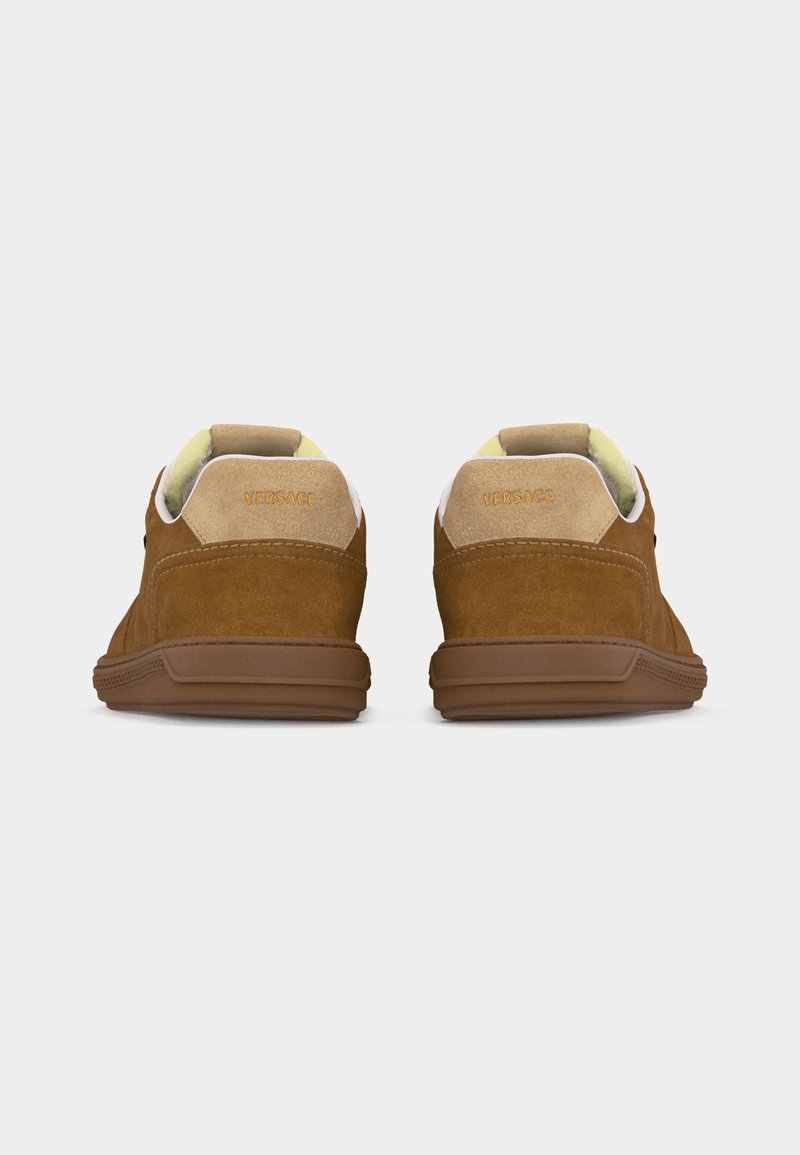 Braune Wildleder-Sneaker mit beigen Fersenschlaufen, gelbem Innenfutter und geprägt versetztem "Versace"-Logo auf der Rückseite, von hinten gezeigt.
