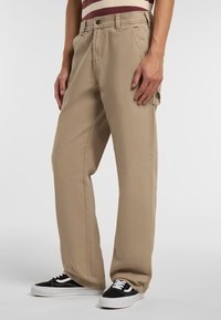 Béžové kalhoty širokého střihu vyrobené z bavlny, s předním zapínáním na knoflík, poutky na opasek a bočními kapsami. V kombinaci s černobílými teniskami.