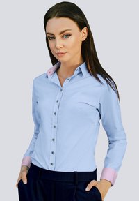 Light blue button-up shirt with a pink collar, featuring black buttons and long sleeves, paired with a dark pinstriped pant.
