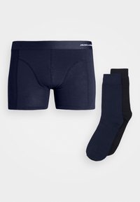 Pantaloni boxer navy con una superficie liscia e una cintura elastica, abbinati a due calzini: uno navy e uno nero, entrambi con un design semplice.
