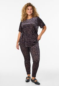 Ensemble haut et legging en imprimé léopard noir et marron, fabriqué en tissu lisse, avec des manches courtes et une coupe décontractée, associé à des ballerines noires.