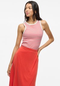 Top sin mangas a rayas en blanco, rojo y beige, combinado con una falda larga roja sólida. Tejido suave, corte relajado, escote redondeado.