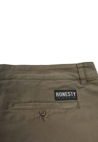 Khakihose mit einer Gesäßtasche, die ein schwarzes Etikett mit "HONESTY RULES", gestickten Details und einem Knopfverschluss aufweist. Strapazierfähiger Stoff.