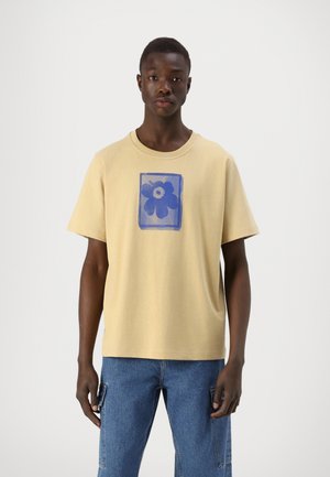 T-shirt en coton jaune à manches courtes avec un design graphique de fleur bleue dans un carré. Coupe décontractée et col rond.
