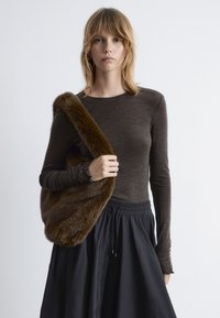 Brown long-sleeve top paired with a black skirt, holding a faux fur bag with a rich texture and deep brown color.