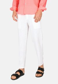 Pantaloni bianchi in lino con una vestibilità rilassata, dotati di tasche laterali e abbinati a sandali neri. Il look è completato da una camicia corallo.