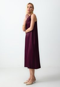 Robe sans manches en satin bordeaux avec une coupe décontractée, longueur au genou et un éclat subtil. Associée à des escarpins nude à bout pointu.