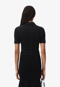 Suéter negro de textura con mangas cortas y cuello, combinado con una falda negra ajustada de canalé. La parte trasera presenta un diseño ligeramente corto.