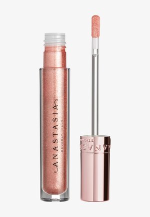 Lucidalabbra in un tubetto trasparente con un cappuccio metallico rosa, caratterizzato da una tonalità scintillante di rosa pesca e da un applicatore corto e affusolato.