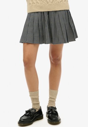 Gonna plissettata a quadri blu navy e beige con taglio svasato, abbinata a scarpe nere e calzini crema a coste per un contrasto di texture.