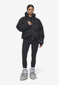 Svart puffjacka med hög krage, med en framzip och överdimensionerad silhuett. Matchas med svarta leggings och gråa snörstövlar.