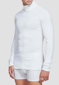 Maglione a maniche lunghe bianco con collo alto realizzato in materiale morbido, design aderente, texture liscia, abbinato a pantaloni boxer bianchi.