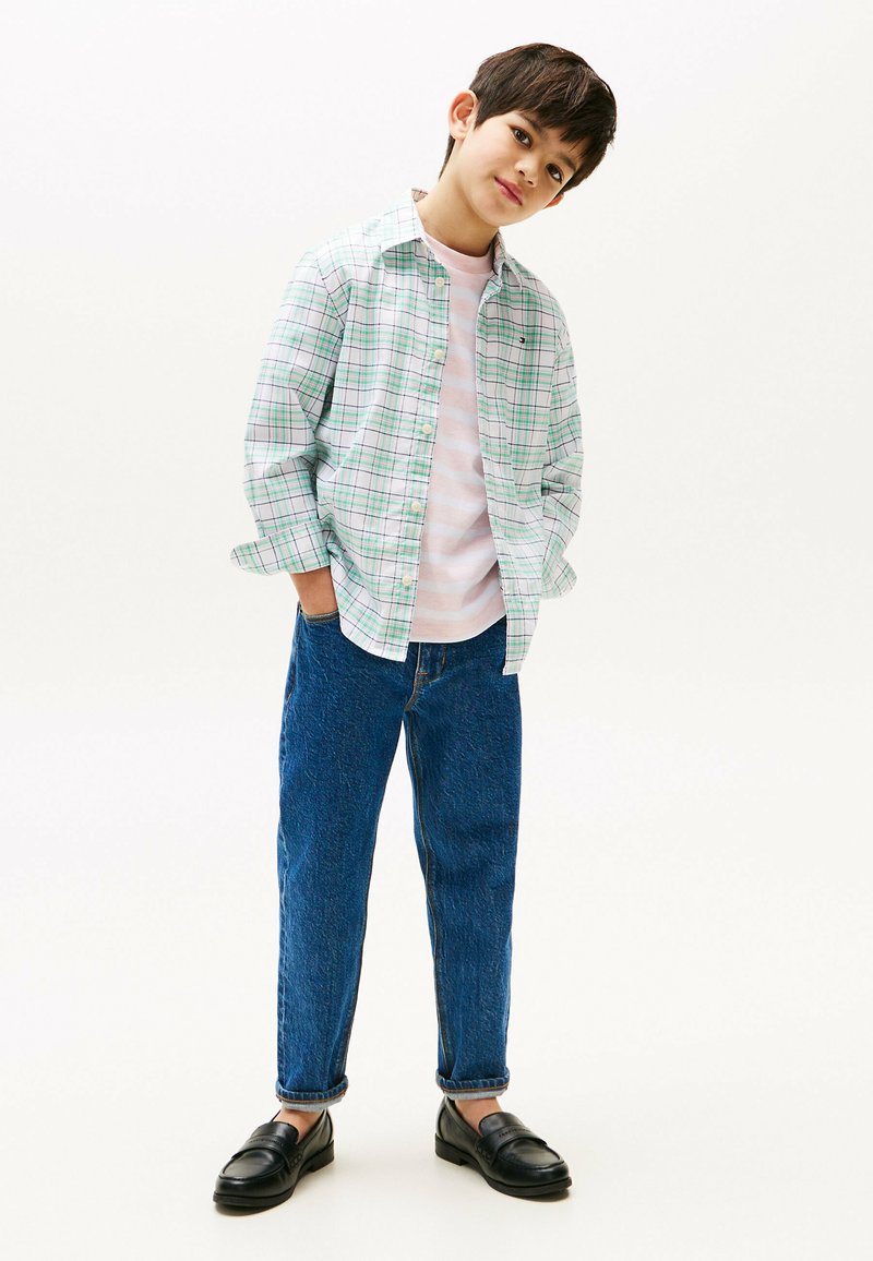 Camicia a quadri verde e bianca sopra una t-shirt a righe rosa; jeans in denim blu e mocassini neri; vestibilità casual.