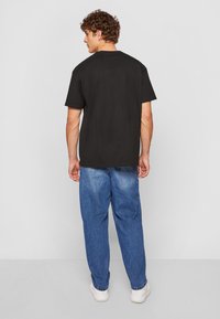 Schwarzes Baumwoll-T-Shirt mit lockerer Passform, kombiniert mit hellblauen Jeans. Die Jeans haben eine ausgewaschene Textur und elastische Bündchen.